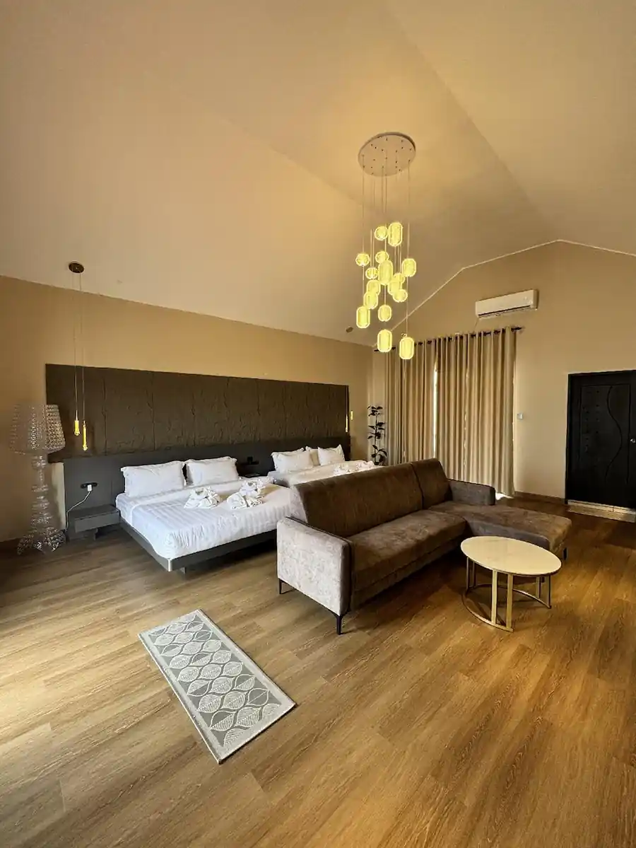 Wide interior view of the Family Deluxe room at Turtle Seaweed Resort featuring a large sectional sofa, comfortable beds, and high ceilings with elegant lighting.
